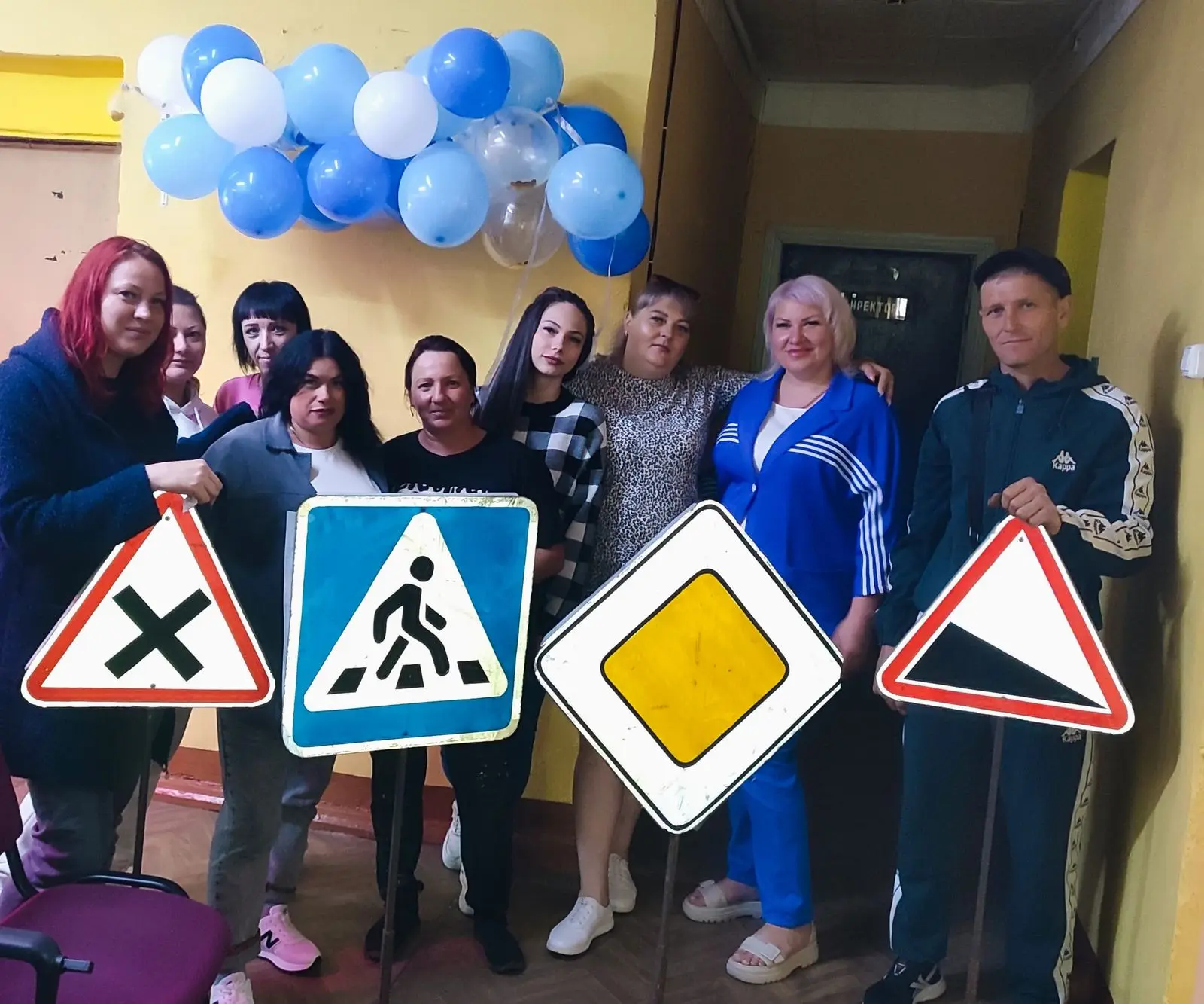 Группа людей с дорожными знаками на фоне голубых и белых шаров